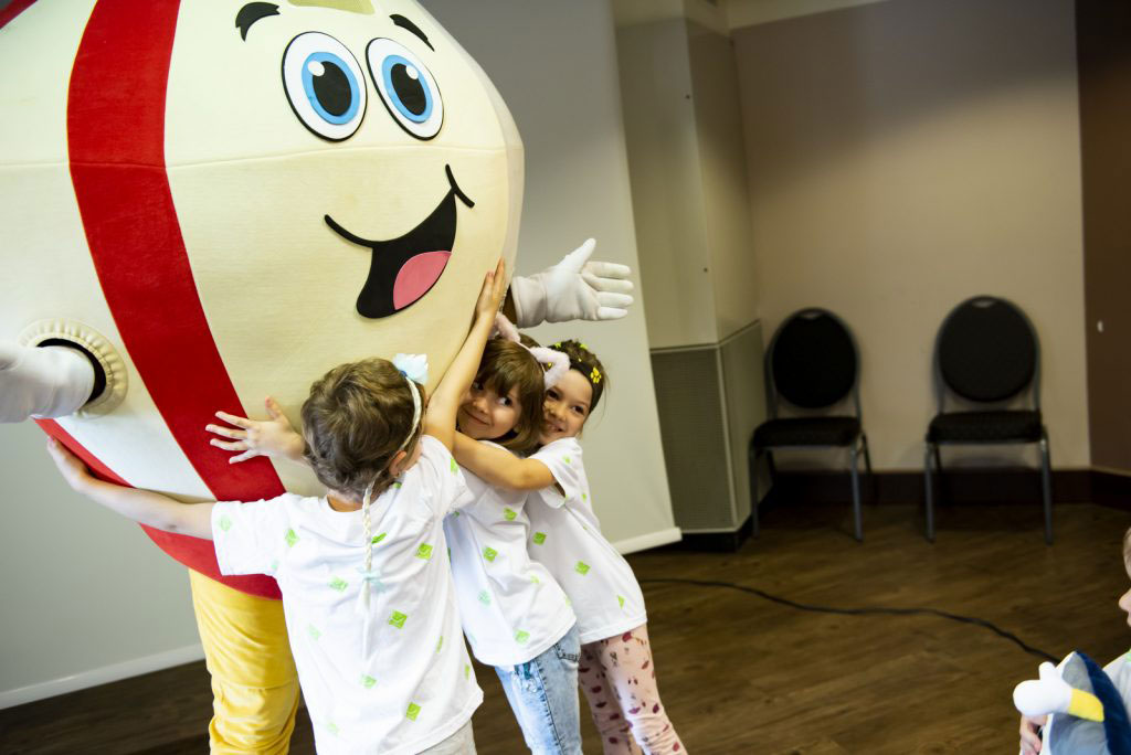 Fotografia przedstawia strój reklamowy w postaci diamentu witający się i obejmowany przez dzieci 